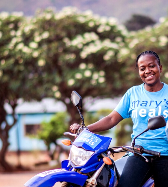 Eine Schulverpflegungsbeauftragte lehnt sich an ihrem Motorrad in Sambia aus.